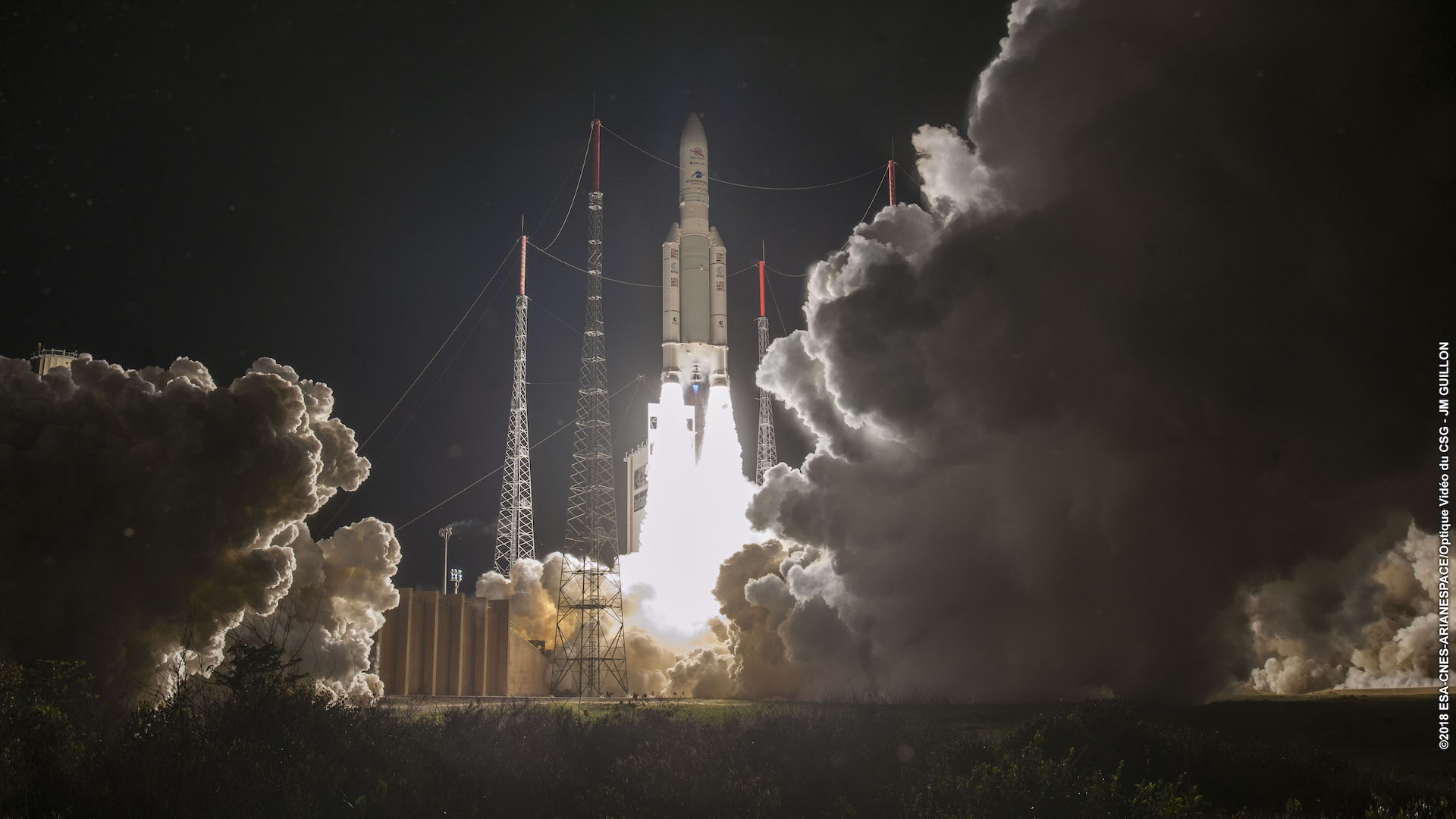 Ariane 5 roketi gecenin karanlığında havalanırken, iki yan iticisi kör edici beyaz bir ateş püskürtüyor, fırlatma rampasından bir duman bulutu yükseliyor