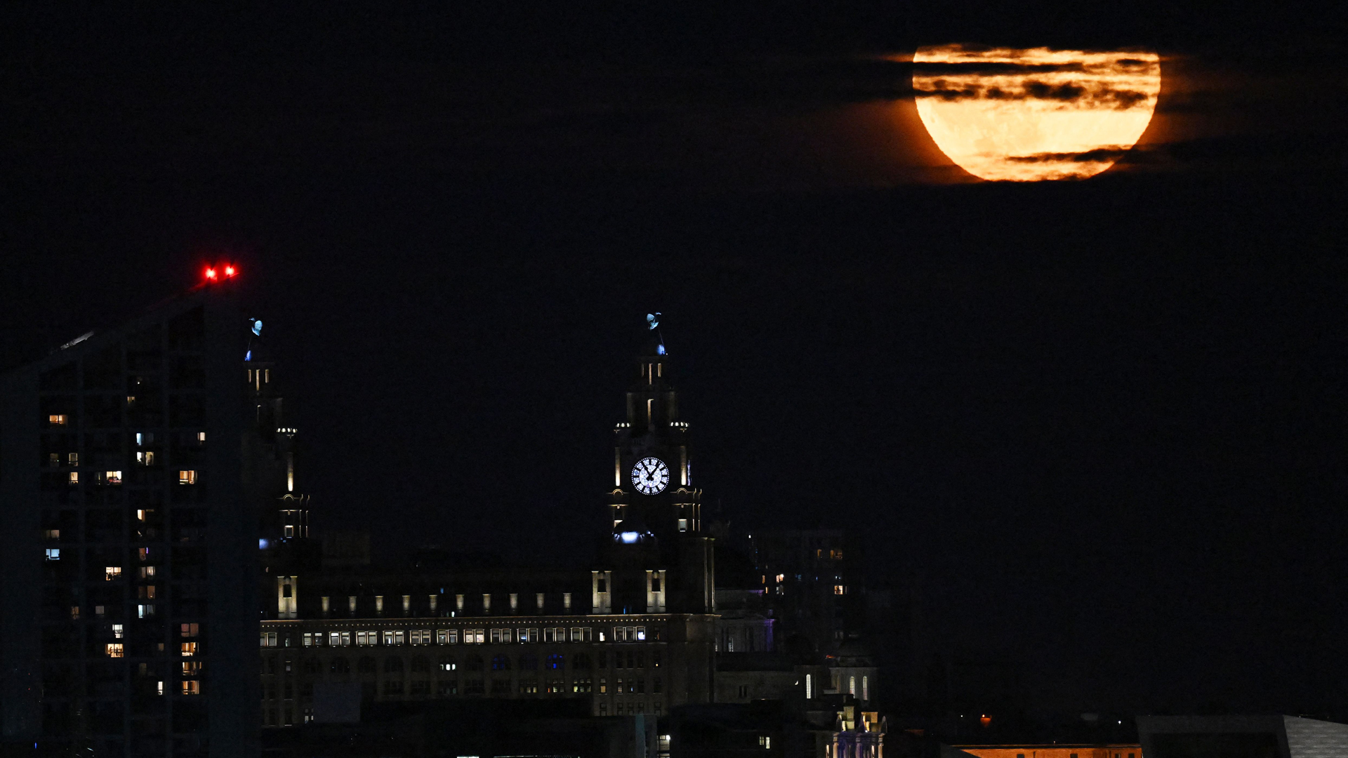 Buck Moon süper ayı, 3 Temmuz 2023'te Liverpool'un tarihi rıhtımları ve Liver Binası üzerindeki kara bulutların arasından parlıyor.